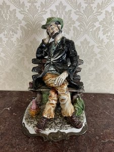 Porcelánová soška muža na lavičke s fliaš vína